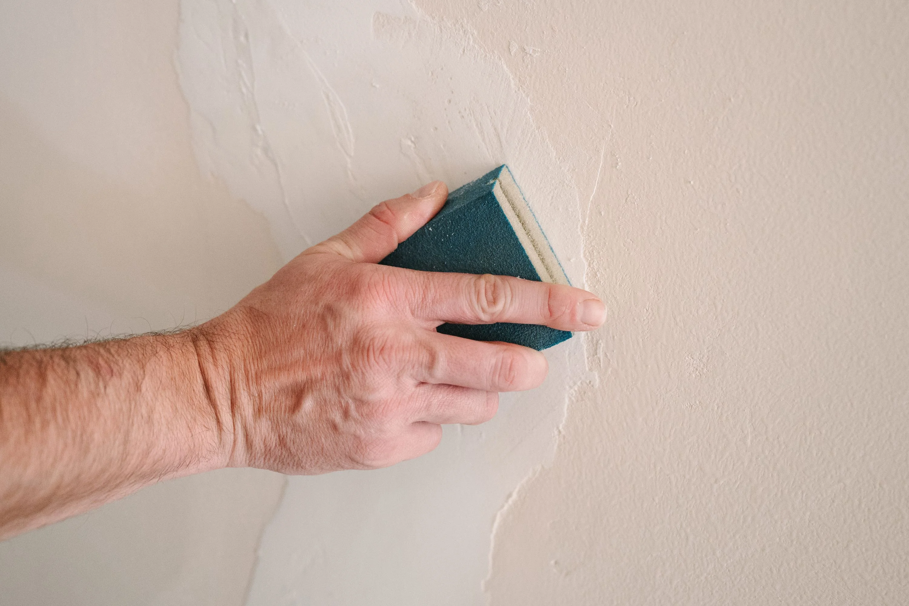Worker sanding and preparing a wall surface before painting